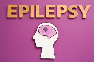 Photo of Human head cutout with brain near word Epilepsy made of wooden letters on purple background, flat lay