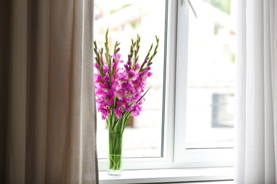 Photo of Vase with beautiful pink gladiolus flowers on windowsill, space for text