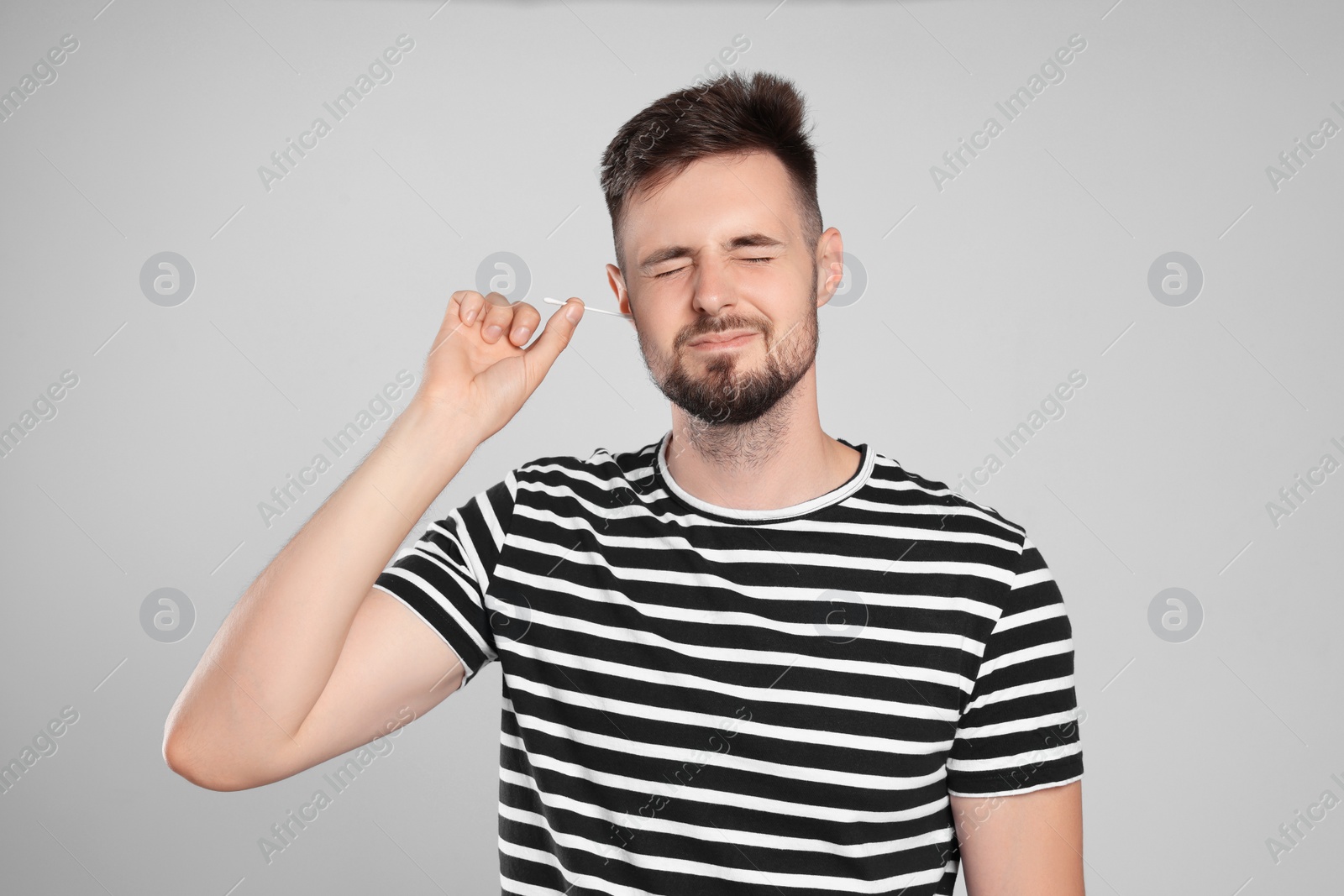 Photo of Young man cleaning ear with cotton swab on light grey background