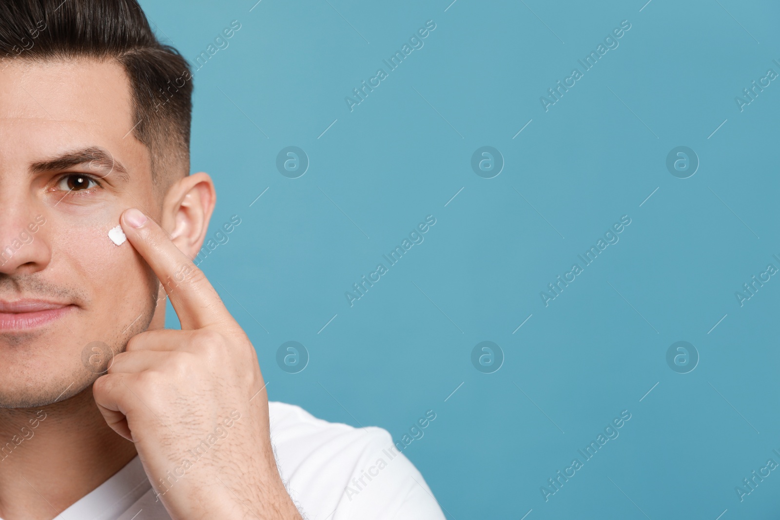 Photo of Handsome man applying face cream against turquoise background, closeup. Space for text