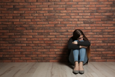 Upset teenage girl sitting on floor near wall. Space for text