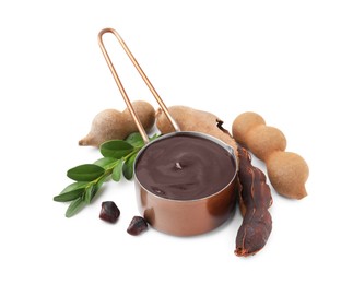 Photo of Measuring cup with tasty tamarind sauce, leaves and fresh pods isolated on white