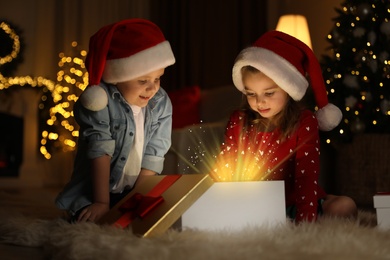 Photo of Cute children opening gift box in room decorated for Christmas