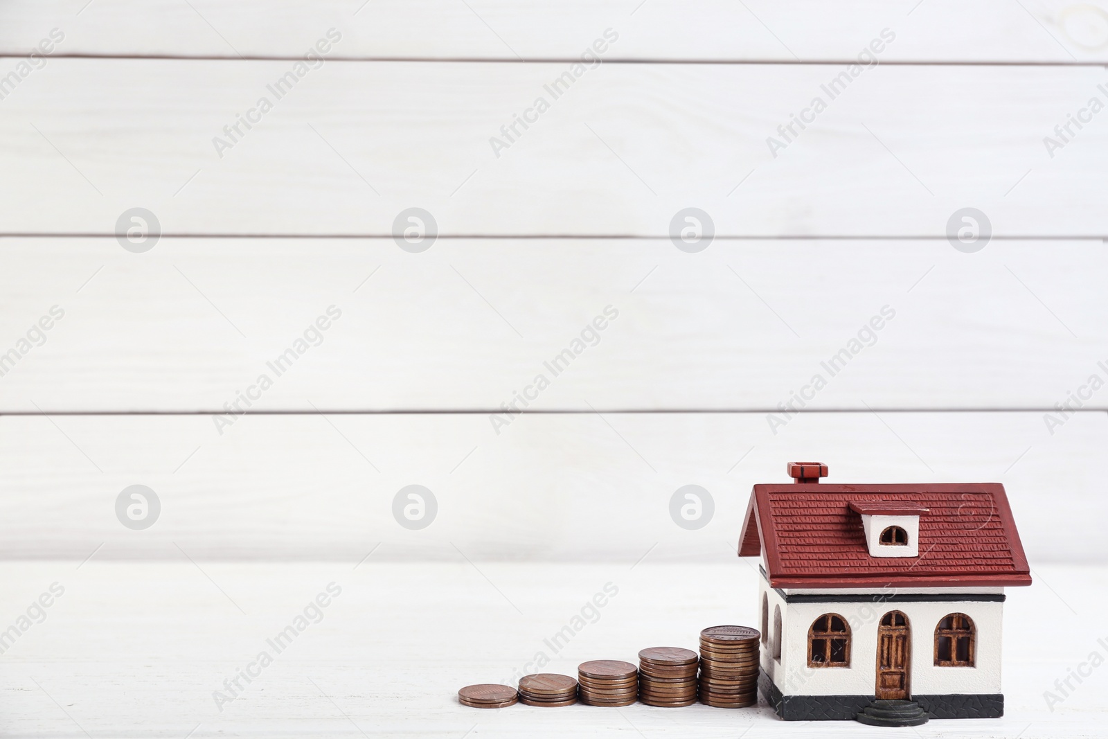 Photo of House model and coins on white wooden table. Space for text