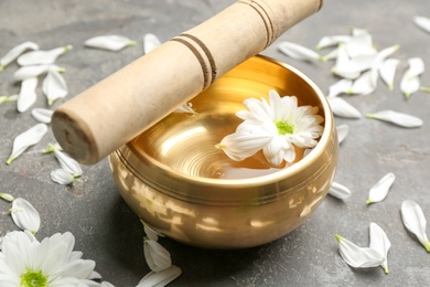 Golden singing bowl with flower and mallet on grey table, closeup. Sound healing