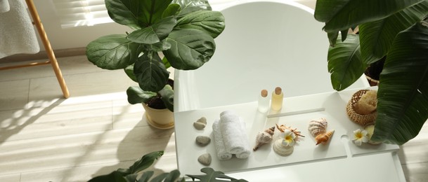 Photo of Bath tray with spa products, towels and shells on tub in bathroom, above view. Space for text