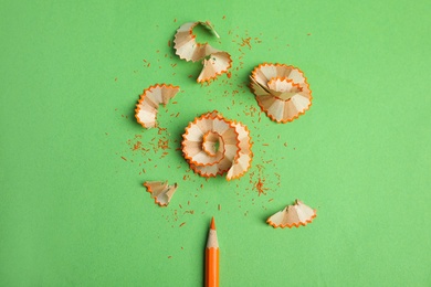 Photo of Color pencil and shavings on green background, top view