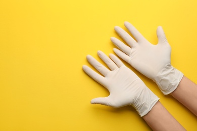 Photo of Person in medical gloves on yellow background, top view. Space for text