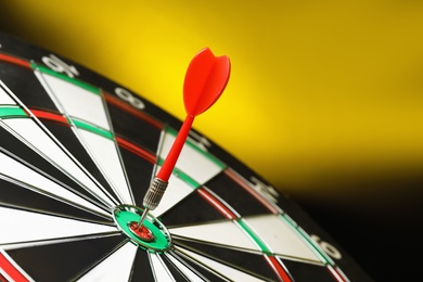 Photo of Red arrow hitting target on dart board against yellow background. Space for text