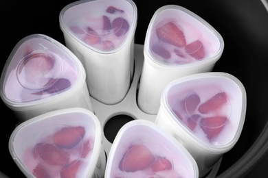 Photo of Cups of homemade strawberry yogurt in modern multi cooker, closeup view