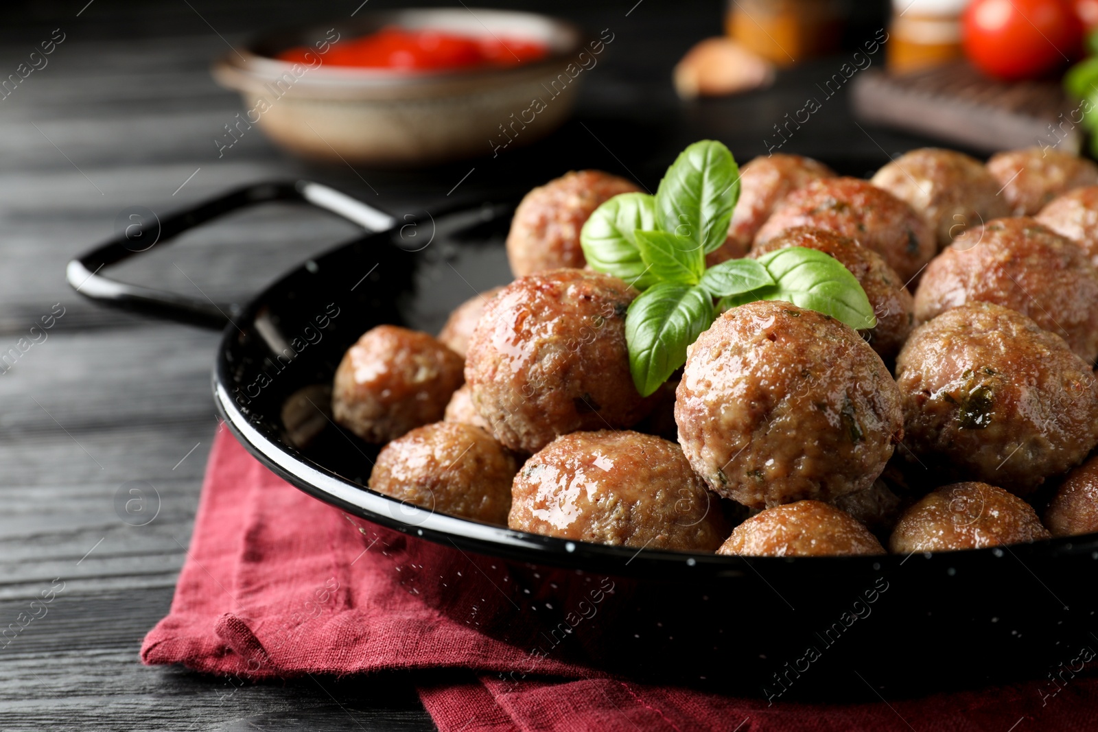 Photo of Tasty cooked meatballs with basil on black wooden table, closeup