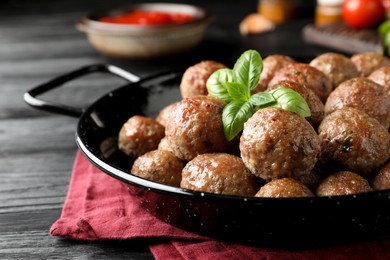 Photo of Tasty cooked meatballs with basil on black wooden table, closeup