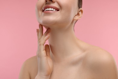 Photo of Smiling woman touching her neck on pink background, closeup