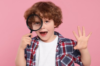 Cute little boy looking through magnifier glass on pink background
