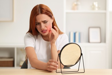 Photo of Suffering from allergy. Young woman with mirror checking her face at home