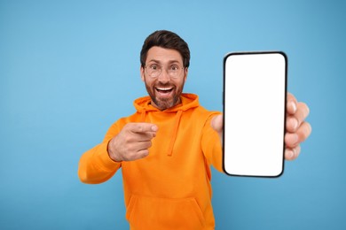 Handsome man showing smartphone in hand and pointing at it on light blue background