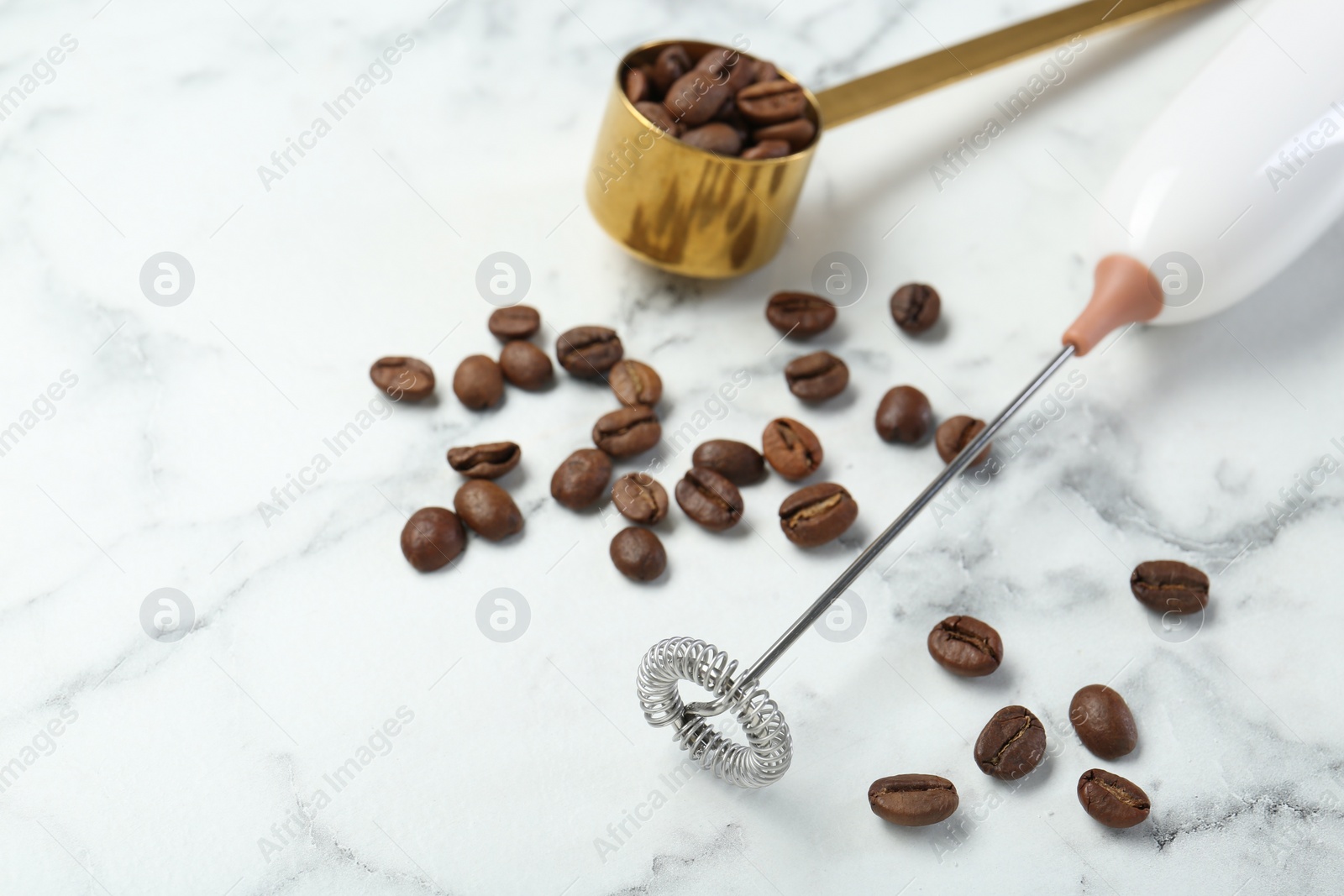 Photo of Milk frother wand and coffee beans on white marble table, closeup. Space for text