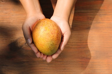 Photo of Woman holding tasty mango at wooden table, top view