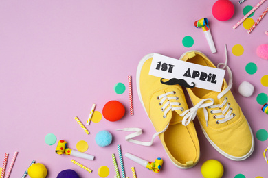 Shoes tied together and note with phrase 1st APRIL on lilac background, flat lay. Space for text