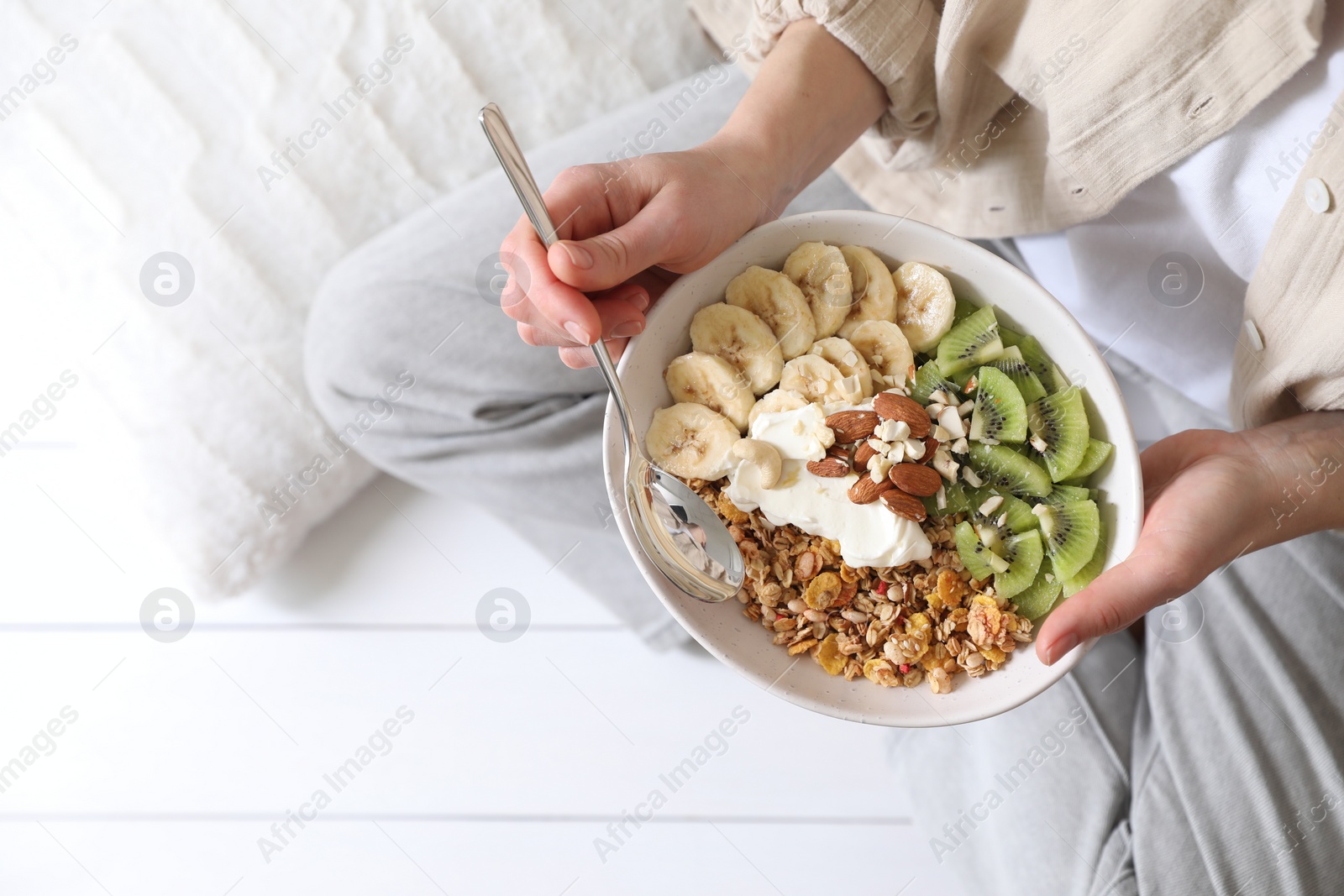 Photo of Woman eating tasty granola indoors, top view