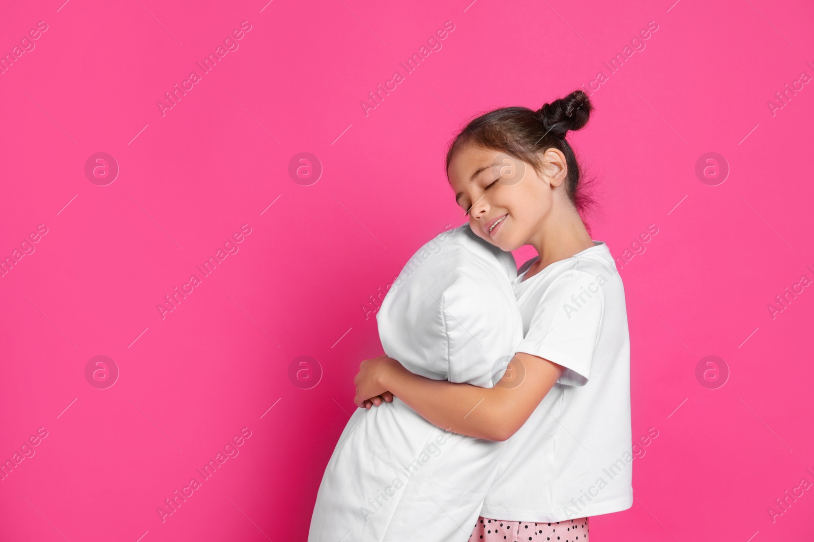 Photo of Cute girl in pajamas hugging pillow on pink background. Space for text