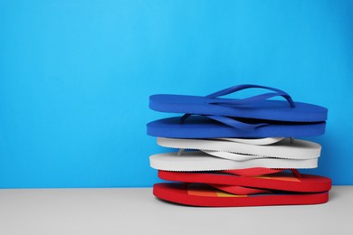 Photo of Stack of different flip flops on white table against light blue background, space for text