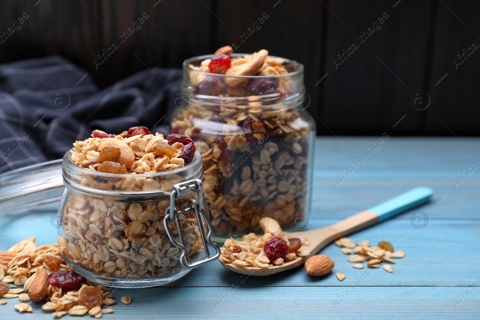 Photo of Jars of tasty granola with nuts and dry fruits on light blue wooden table. Space for text