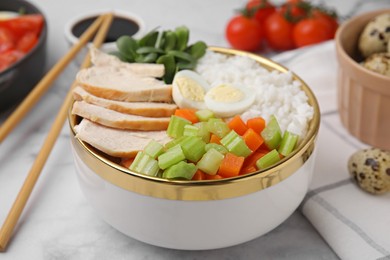 Delicious poke bowl with meat, egg, rice and vegetables served on white marble table, closeup