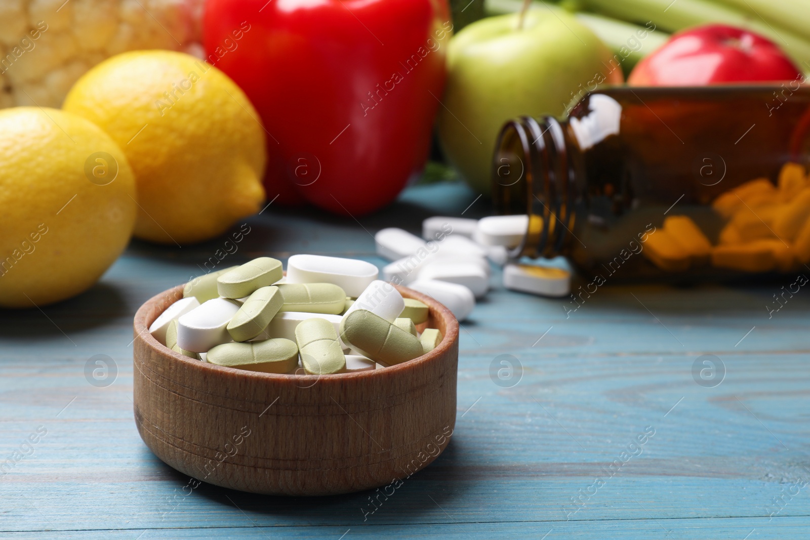 Photo of Dietary supplements. Bowl with different pills near food products on light blue wooden table, closeup