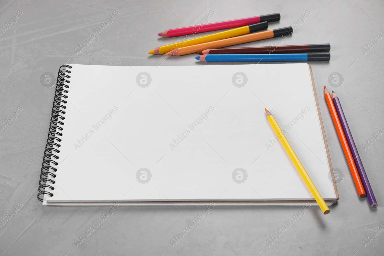 Photo of Empty sketchbook and colorful pencils on grey textured table, above view