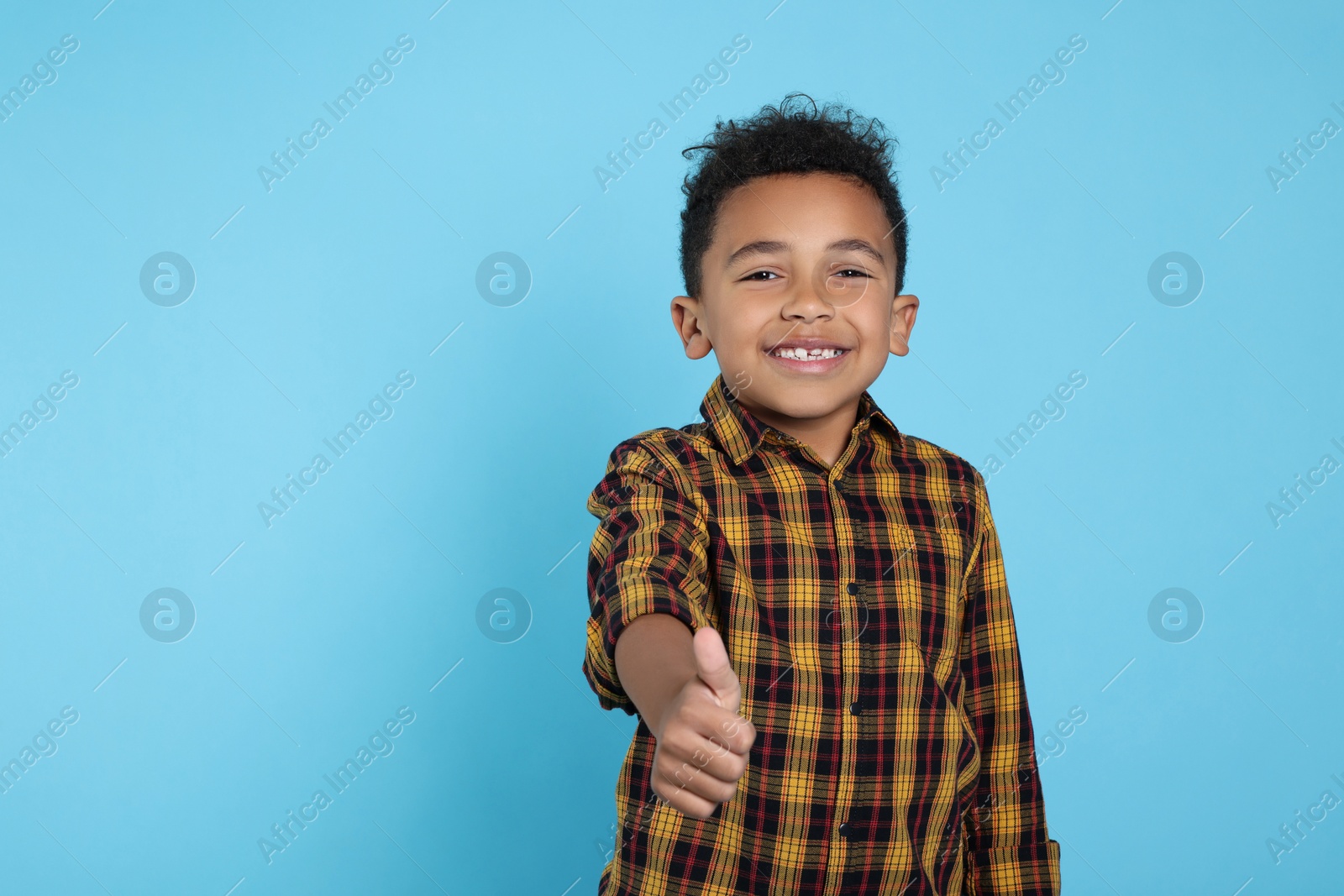 Photo of African-American boy showing thumb up on turquoise background. Space for text