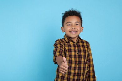 Photo of African-American boy showing thumb up on turquoise background. Space for text