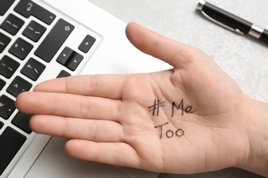 Photo of Woman showing palm with hashtag METOO at laptop on grey background, closeup. Stop sexual assault
