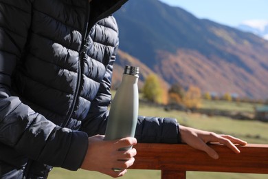 Photo of Boy holding thermo bottle with drink in mountains on sunny day, closeup