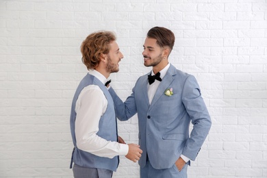 Happy newlywed gay couple in suits against white wall