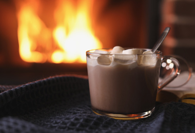 Photo of Delicious sweet cocoa with marshmallows and blurred fireplace on background