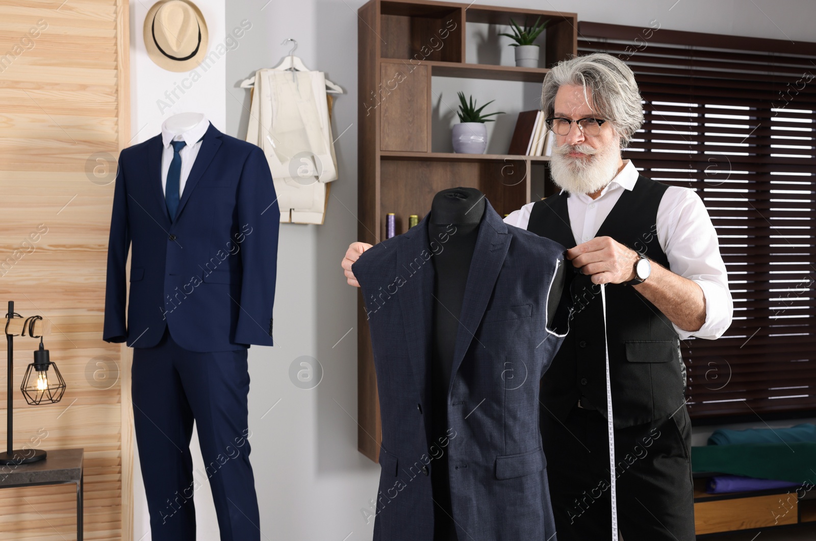 Photo of Professional tailor with measuring tape working in atelier