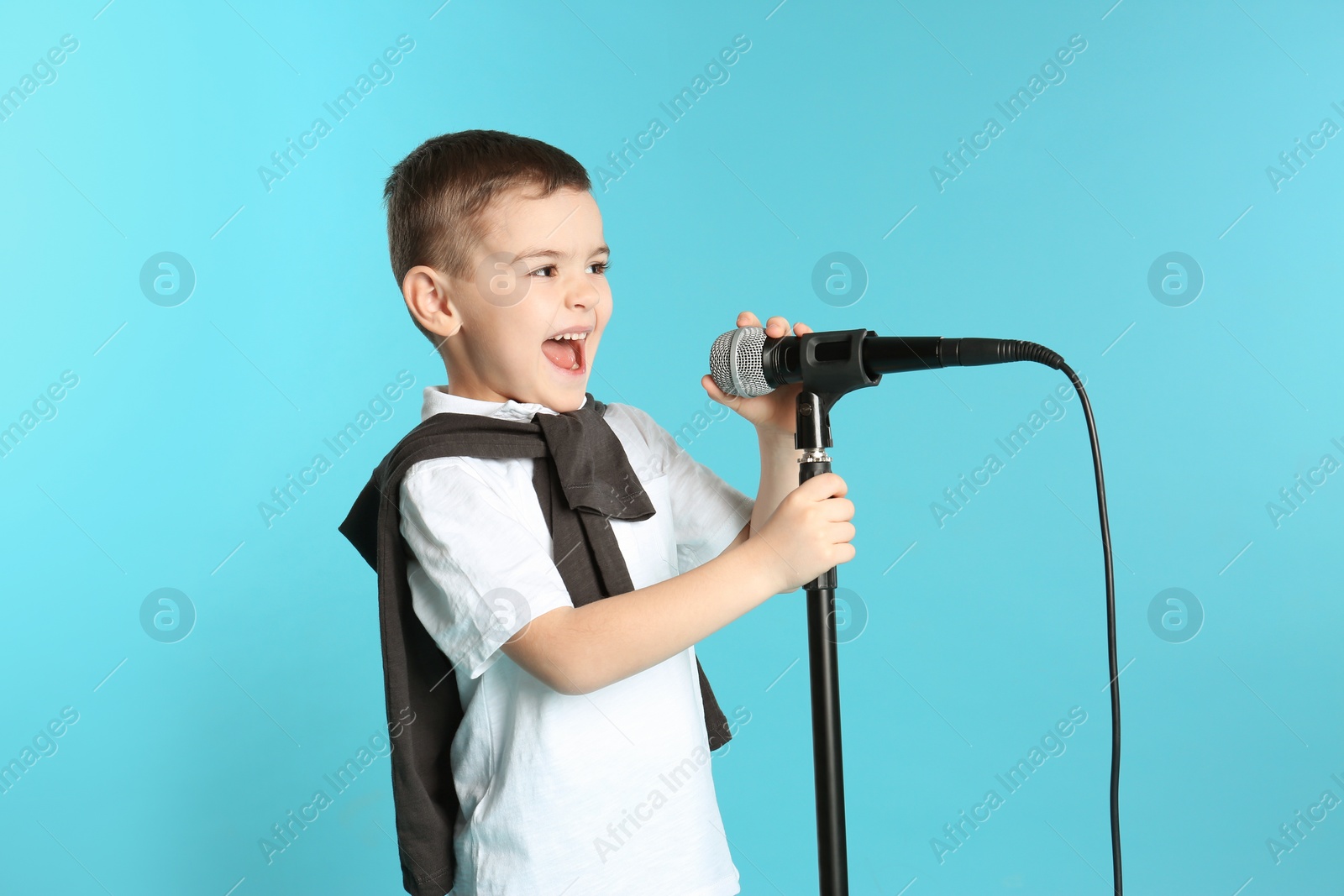 Photo of Cute funny boy with microphone on color background