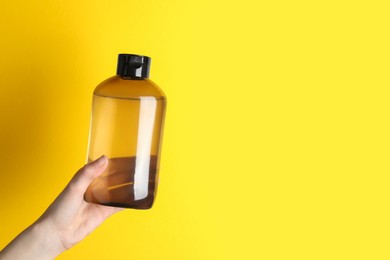 Photo of Woman holding shampoo bottle on yellow background, closeup. Space for text