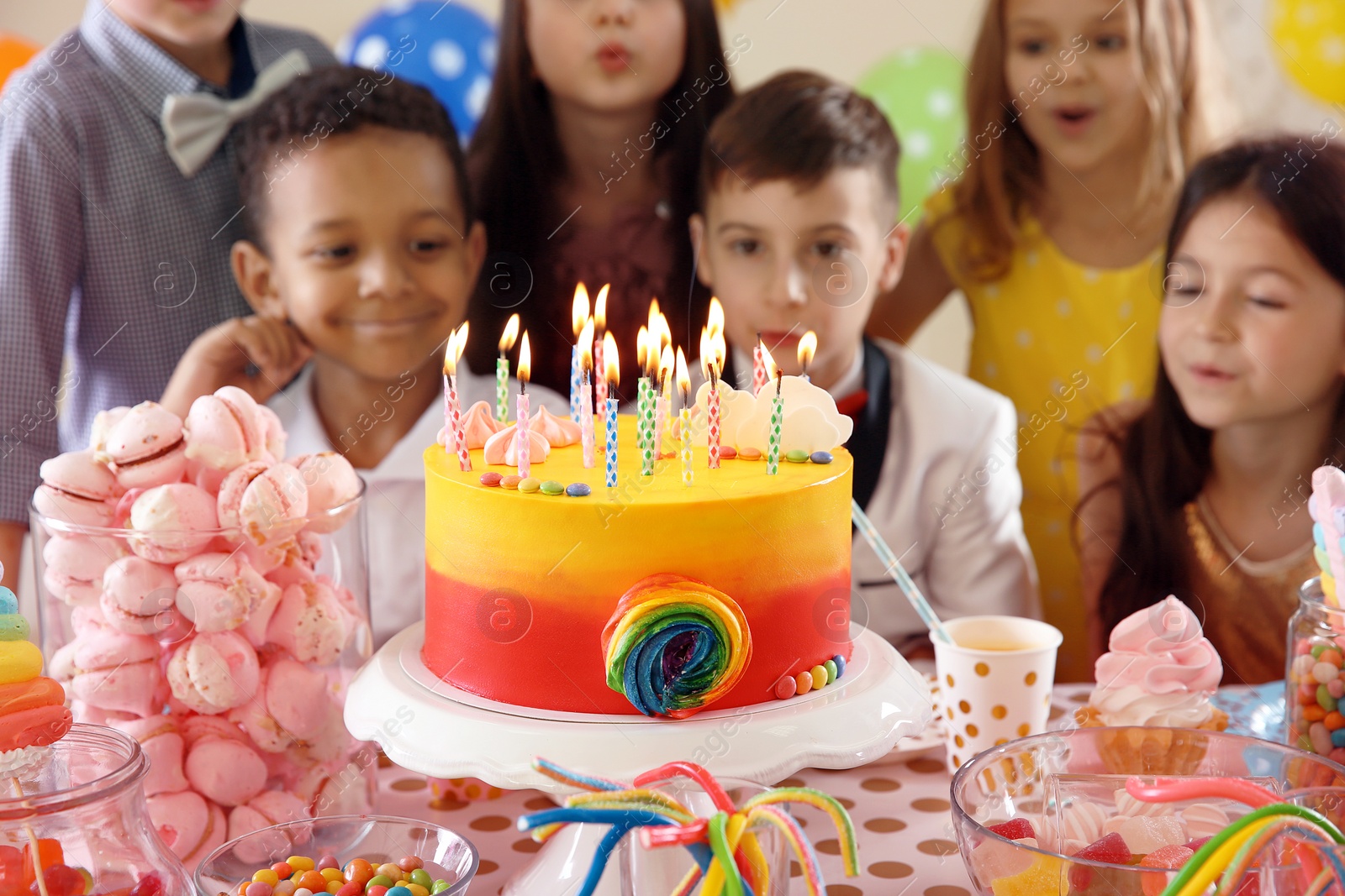 Photo of Cute children blowing out candles on birthday cake at table indoors