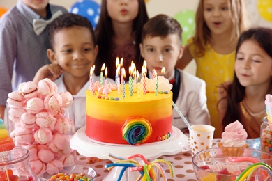 Photo of Cute children blowing out candles on birthday cake at table indoors