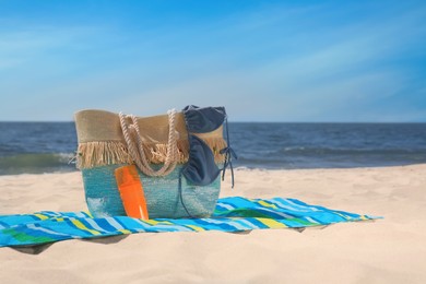 Photo of Striped beach towel and bag with accessories on sandy seashore