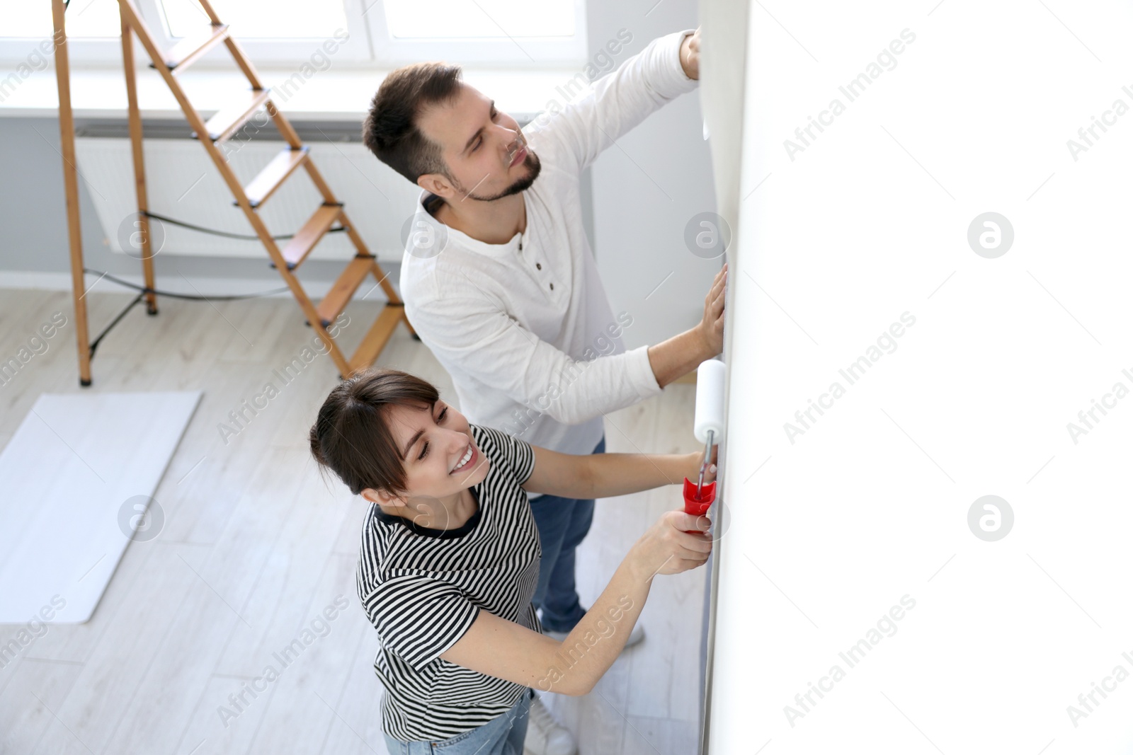 Photo of Woman and man hanging wallpaper in room