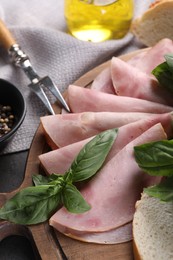 Photo of Tasty ham with basil, bread and carving fork on table, closeup