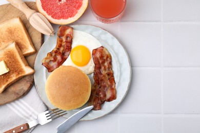 Photo of Tasty pancakes with fried egg and bacon served on white tiled table, flat lay. Space for text