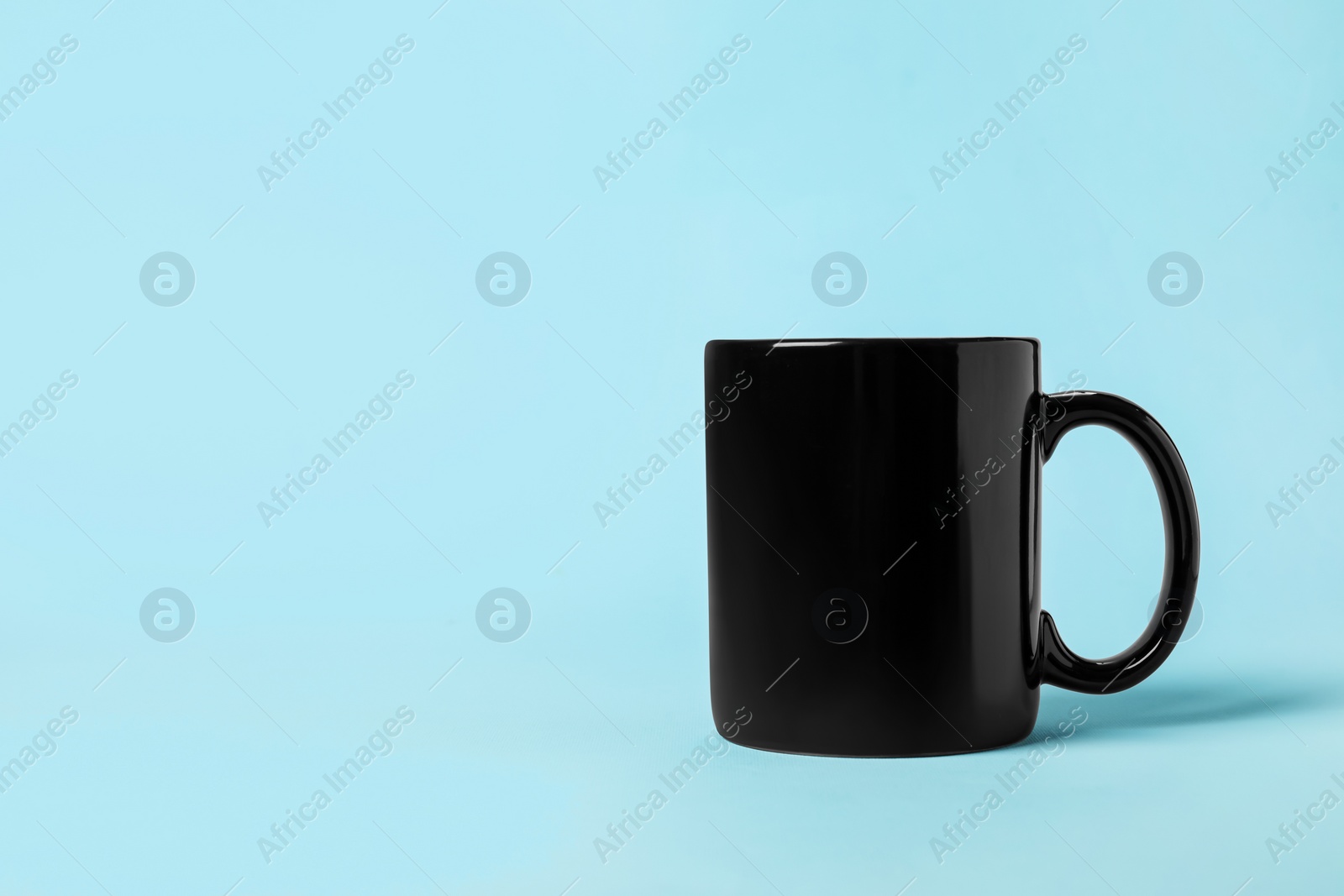 Photo of One black ceramic mug on light blue background, space for text