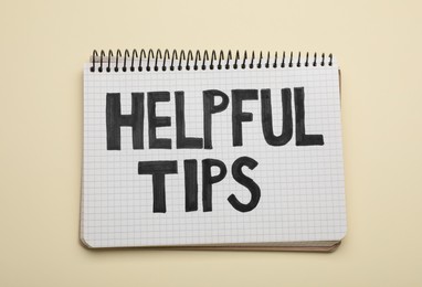 Photo of Phrase Helpful Tips in notebook on beige background, top view