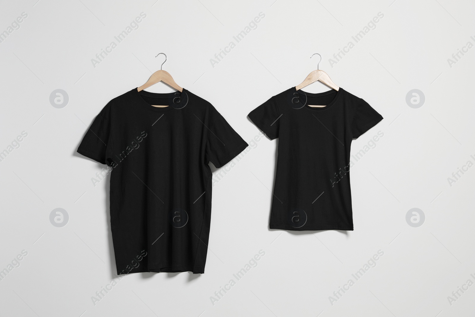 Photo of Hangers with different t-shirts on light wall. Mockup for design