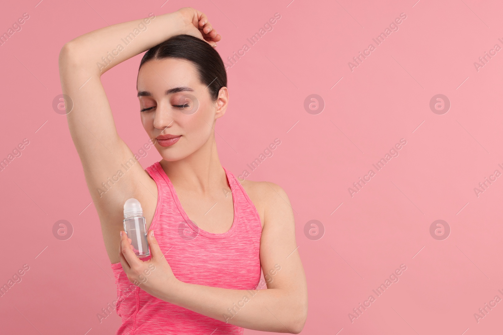 Photo of Beautiful woman applying deodorant on pink background, space for text