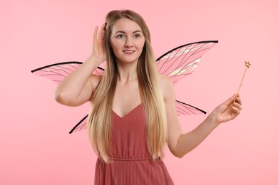Beautiful girl in fairy costume with wings and magic wand on pink background